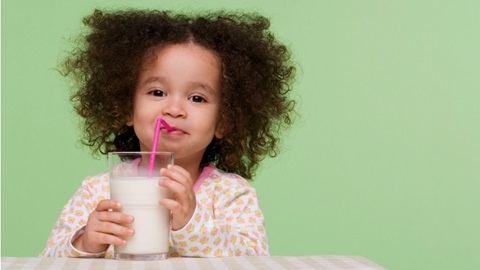 Une fillette, paille en bouche, tient un verre rempli de lait de croissance